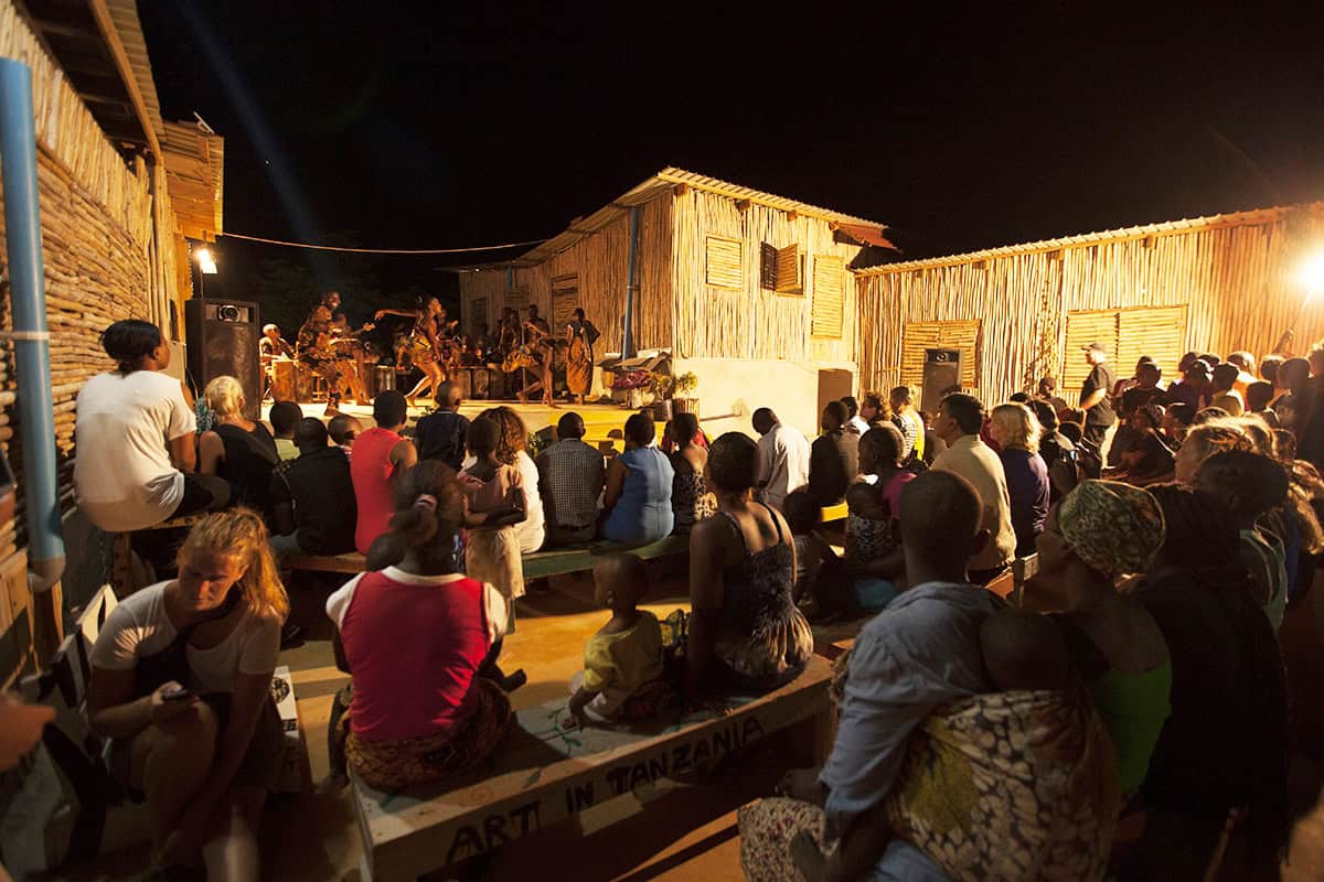 A group of people attending an evening gathering under ambient lighting near wooden structures.