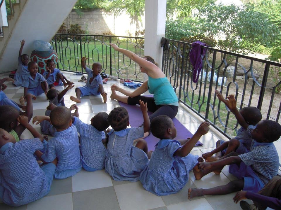 A group of children participating in a yoga session led by a volunteer, showcasing Green Works Africa's volunteering and internship programs focused on village education and sports development.