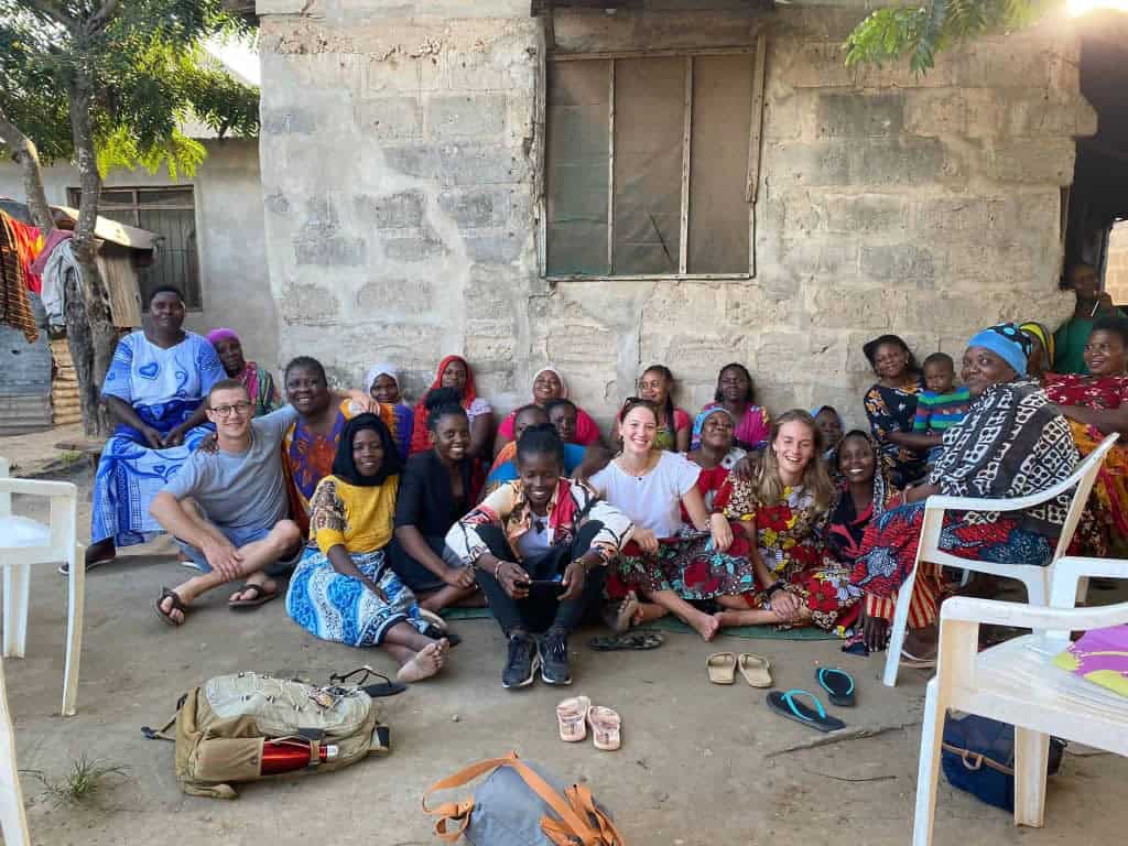 Volunteers sitting with women and children in a Tanzanian community, participating in a social sector program focused on empowerment and education
