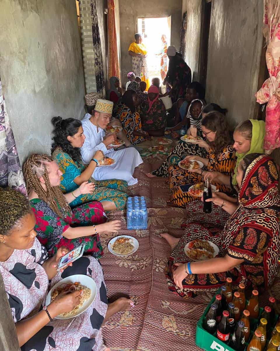 A group of women and volunteers sharing a meal during a community-based social sector volunteering activity in Tanzania.